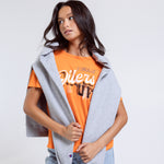 Woman wearing an orange t-shirt with text, gray cardigan, and blue jeans on a white background