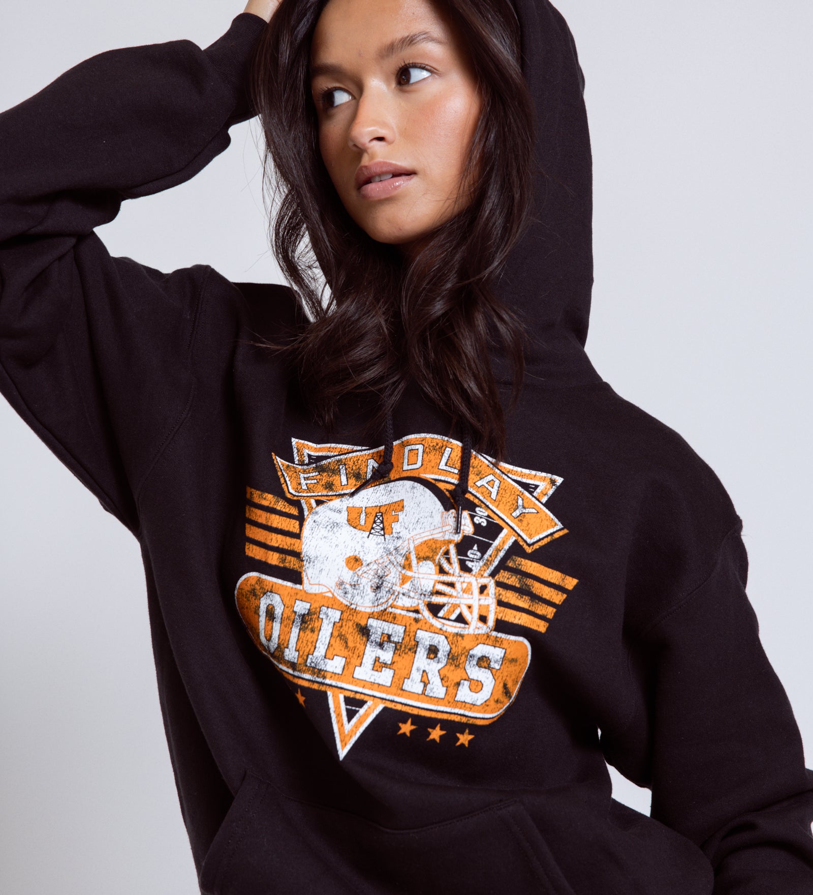 Person wearing a black hoodie with a sports team logo on a plain background