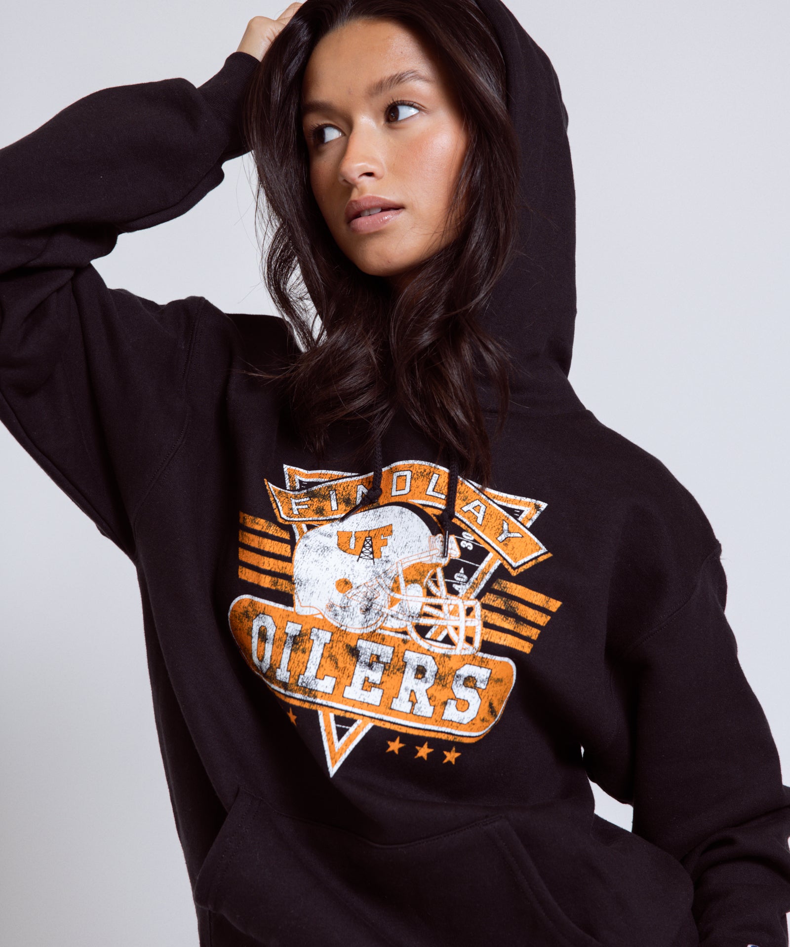 Person wearing a black hoodie with a sports team logo on a plain background