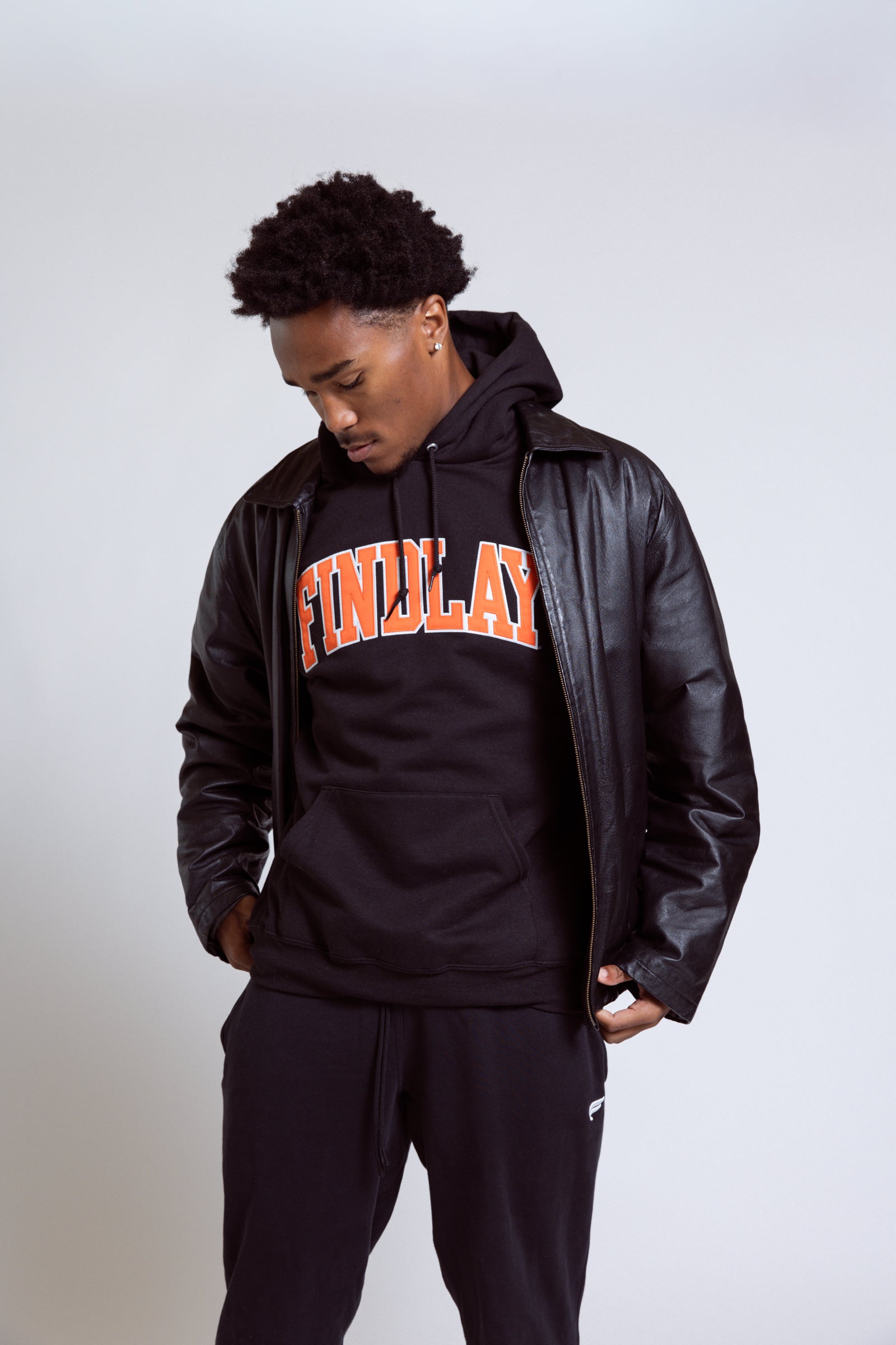 Person wearing a black hoodie with 'FINELAND' text and a leather jacket on a plain background